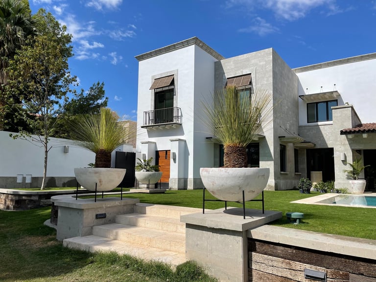Modern white residential house with contemporary architecture, manicured garden, and pool area under blue sky